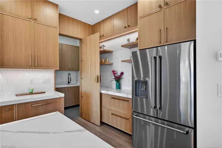 Kitchen featuring high end refrigerator, open shelves, tasteful backsplash, dark wood finished floors, and light stone countertops