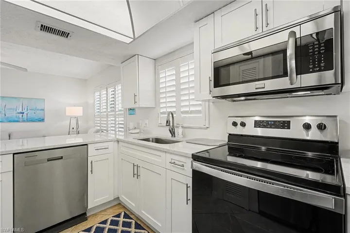 Kitchen featuring appliances with stainless steel finishes, white cabinets, open floor plan, and light stone counters