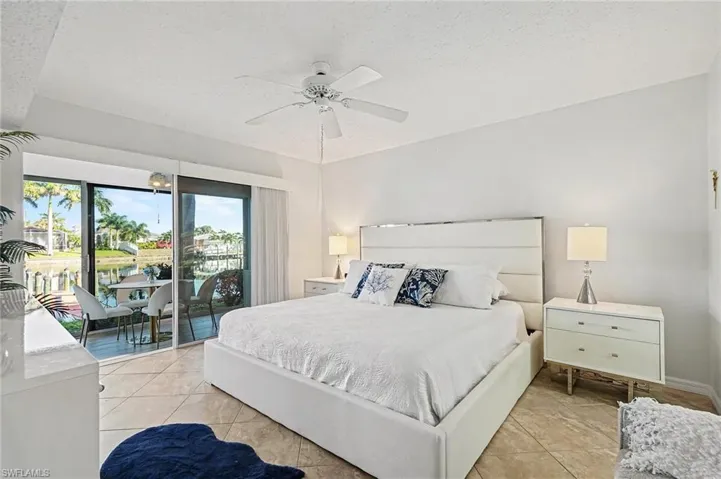 Bedroom with a textured ceiling, access to exterior, light tile patterned flooring, a ceiling fan, and a water view