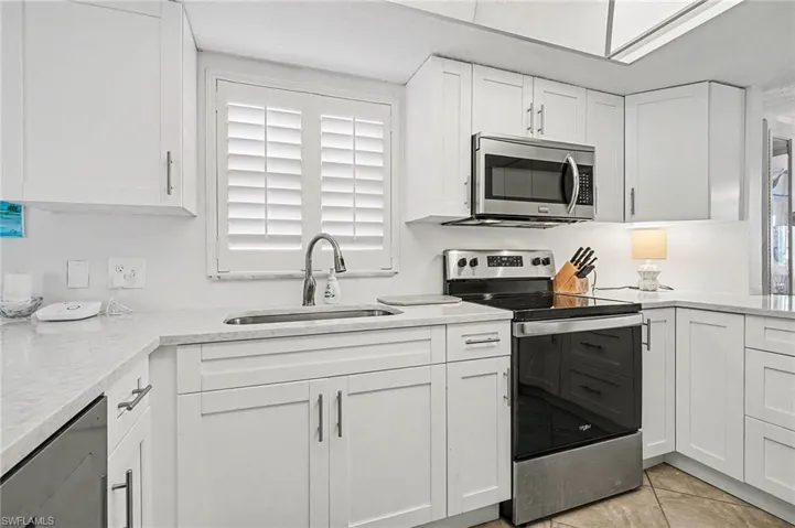 Kitchen with stainless steel appliances, light stone counters, white cabinets, and light tile patterned floors