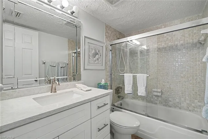 Bathroom with combined bath / shower with glass door, a textured ceiling, and vanity
