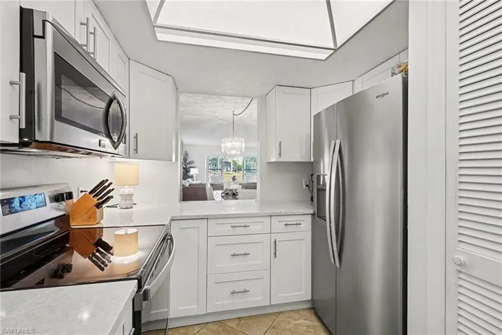 Kitchen featuring appliances with stainless steel finishes, white cabinets, a chandelier, light stone counters, and light tile patterned flooring