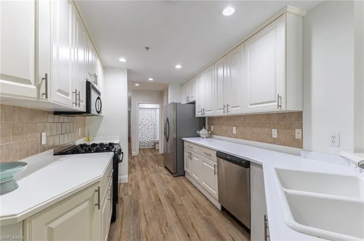 Kitchen with stainless steel appliances, light wood finished floors, light countertops, recessed lighting, and backsplash