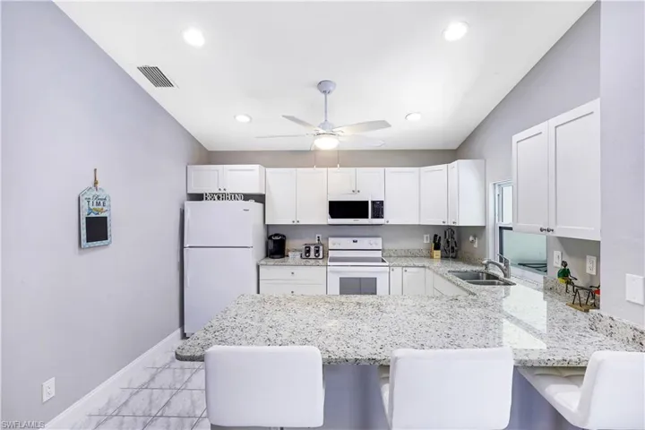Kitchen with white appliances, a kitchen breakfast bar, light stone counters, white cabinets, and vaulted ceiling