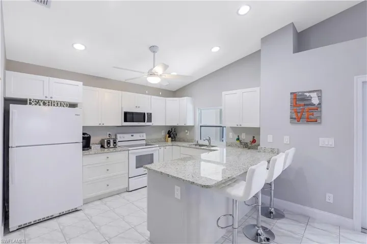Kitchen featuring white appliances, light stone countertops, white cabinetry, a peninsula, and a kitchen bar