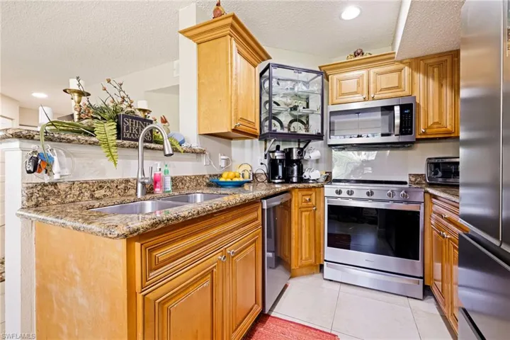 Kitchen with stainless steel appliances, a textured ceiling, stone counters, light tile patterned floors, and brown cabinetry
