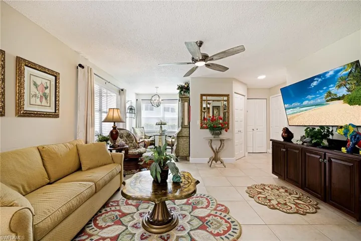 Living room with a ceiling fan, light tile patterned floors, a textured ceiling, and a chandelier