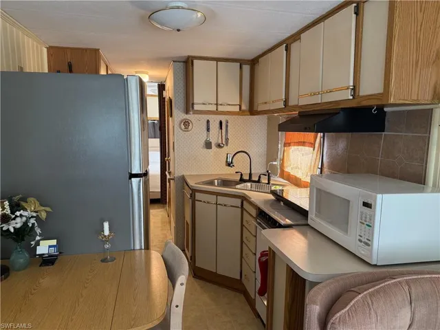 Kitchen featuring freestanding refrigerator, white microwave, wall chimney range hood, backsplash, and light countertops