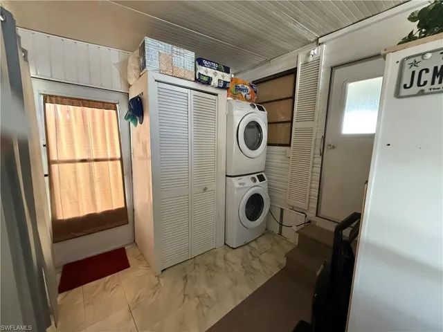 Washroom featuring stacked washer / drying machine and marble look tiles