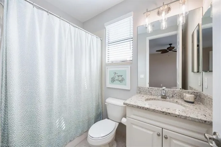 Bathroom featuring toilet, vanity, a shower with shower curtain, and ceiling fan