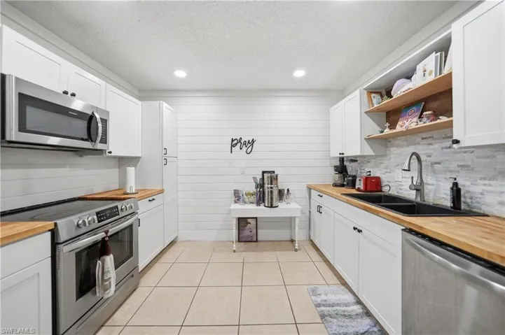 Kitchen with full-height white cabinetry, wood-finish countertops, stainless steel appliances, and tile flooring