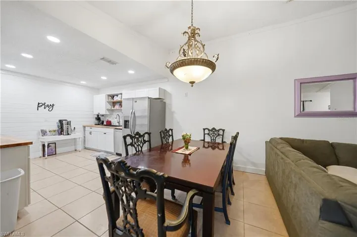 Open-concept space featuring a dining area with a chandelier, a kitchen area with white cabinetry, wood-finish countertops, and stainless steel appliances, and tile flooring throughout