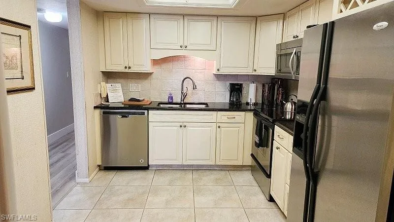 Kitchen with stainless steel appliances, decorative backsplash, white cabinetry, dark stone counters, and light tile patterned floors