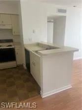 Kitchen featuring range with electric cooktop, light countertops, a peninsula, exhaust hood, and white cabinetry