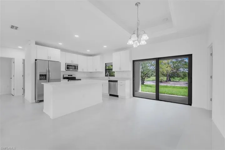 Kitchen featuring white cabinetry, appliances with stainless steel finishes, a kitchen island, decorative light fixtures, and a chandelier