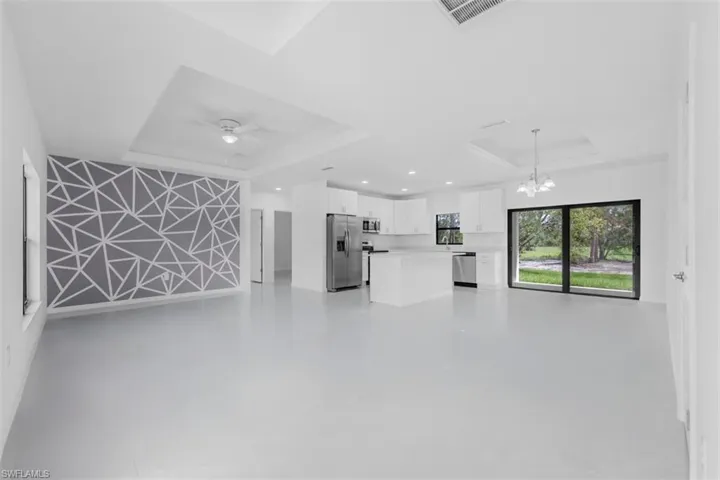 Unfurnished living room with a tray ceiling, a chandelier, and concrete floors