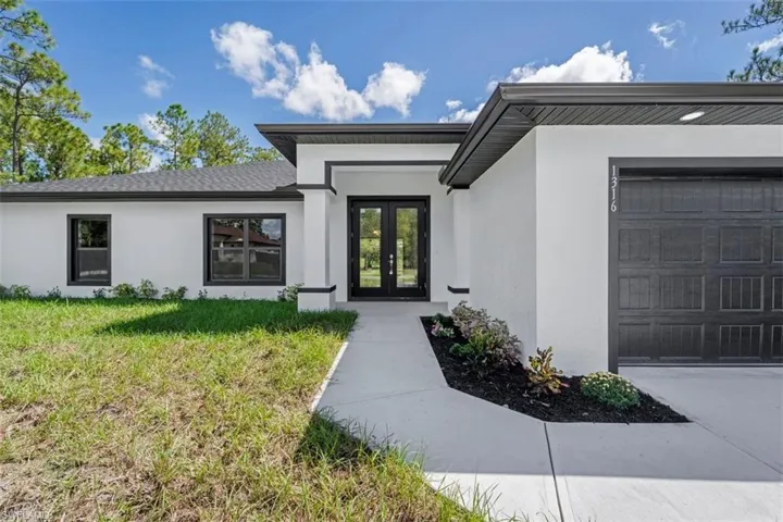 Property entrance featuring french doors, stucco siding, a garage, and a lawn