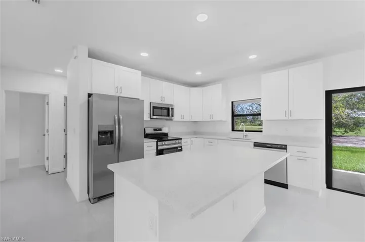 Kitchen featuring stainless steel appliances, white cabinets, light stone countertops, recessed lighting, and a kitchen island