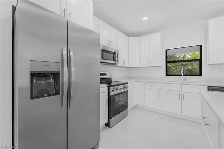 Kitchen with appliances with stainless steel finishes, white cabinets, light tile patterned floors, light stone countertops, and recessed lighting