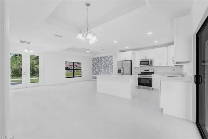 Kitchen featuring open floor plan, a center island, white cabinets, appliances with stainless steel finishes, and light countertops