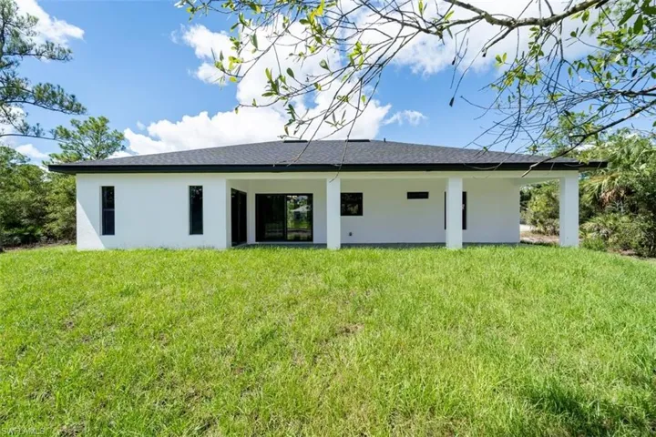 Rear view of house featuring a lawn, stucco siding, a patio, and roof with shingles