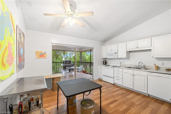 Vaulted ceiling with a ceiling fan, wood-finish flooring, white cabinetry, white appliances, and a screened balcony