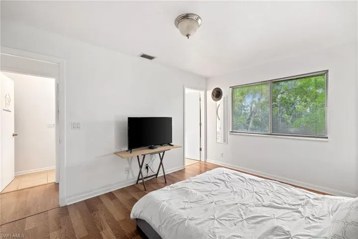 White painted walls, wood-finish flooring, two large windows, white ceiling, and an overhead flush-mount light fixture