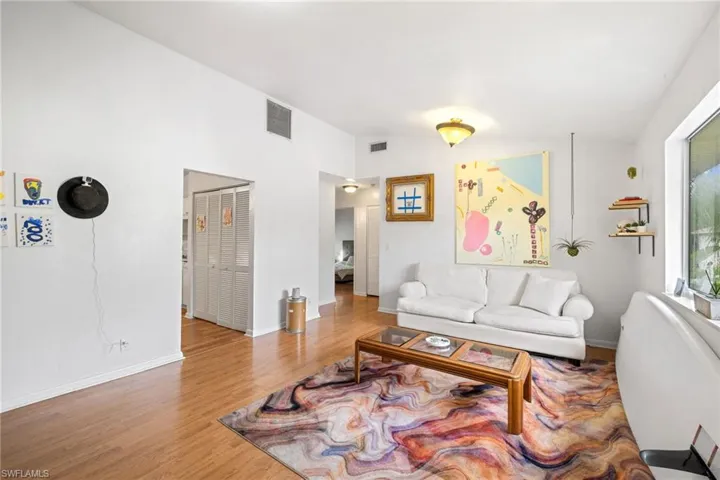 Wood-finish flooring, white walls, vaulted ceiling, recessed lighting, and a large window