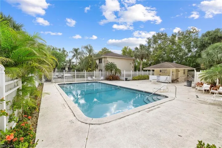 Fenced swimming pool with concrete decking, surrounding tropical landscaping, and an adjacent cabana structure