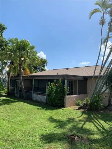 Back of house with stucco siding, a shingled roof, a yard, and a sunroom