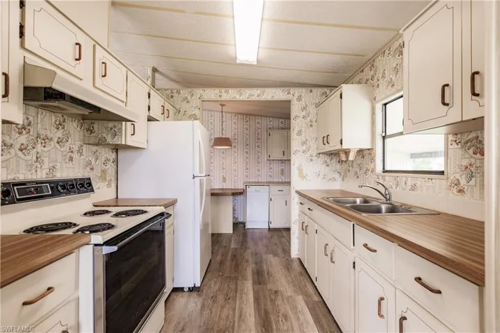 Kitchen with white appliances, sink, lofted ceiling, white cabinetry, and dark hardwood / wood-style flooring