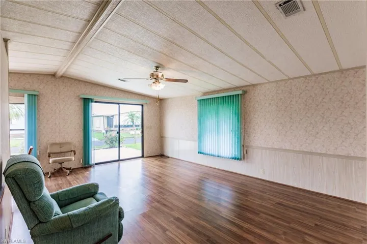 Living room featuring plenty of natural light, lofted ceiling with beams, ceiling fan, and wood-type flooring