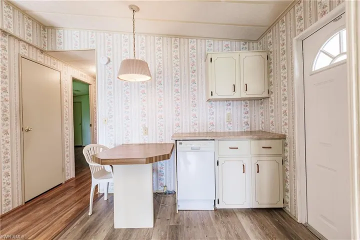 Kitchen with vaulted ceiling, light wood-type flooring, white dishwasher, and decorative light fixtures