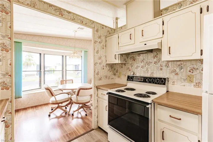 Kitchen with white cabinets, vaulted ceiling, white range with electric stovetop, light wood-type flooring, and a notable chandelier