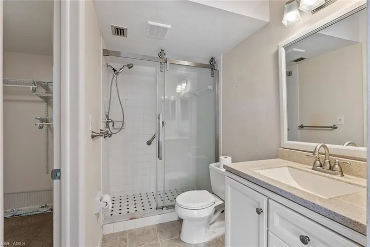 Bathroom with vanity with extensive cabinet space, toilet, tile floors, and a shower with door