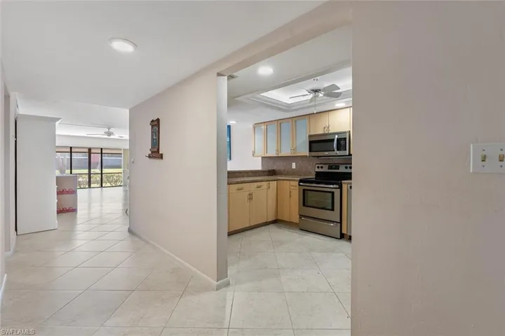 Kitchen with light brown cabinetry, light tile flooring, stainless steel appliances, ceiling fan, and tasteful backsplash