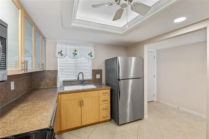 Kitchen featuring ceiling fan, stainless steel fridge, light brown cabinetry, light tile floors, and sink