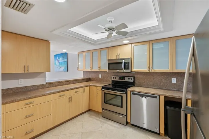Kitchen featuring stainless steel appliances, a tray ceiling, tasteful backsplash, ceiling fan, and light tile floors
