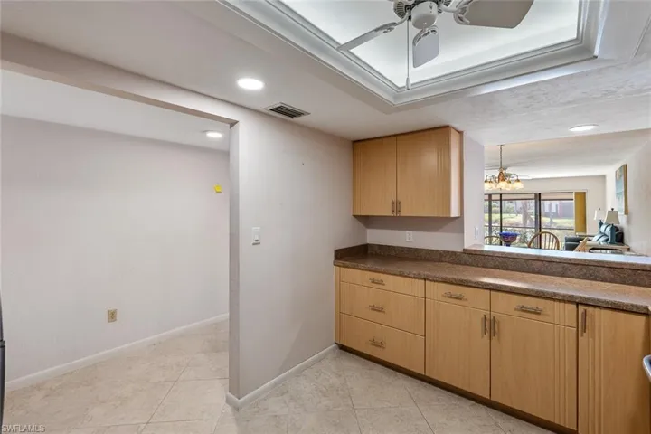 Kitchen featuring hanging light fixtures, light tile flooring, light brown cabinetry, and ceiling fan with notable chandelier