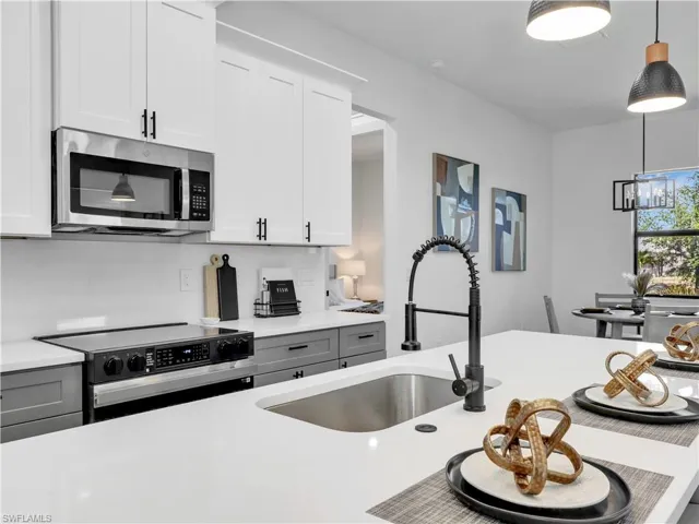 Contemporary kitchen featuring white upper cabinetry, gray lower cabinetry, and stainless steel appliance  photos used from another listing to show what it would look like with furniture