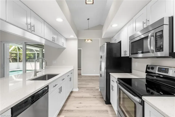 Kitchen with white cabinets, vaulted ceiling, light stone counters, stainless steel appliances, and sink