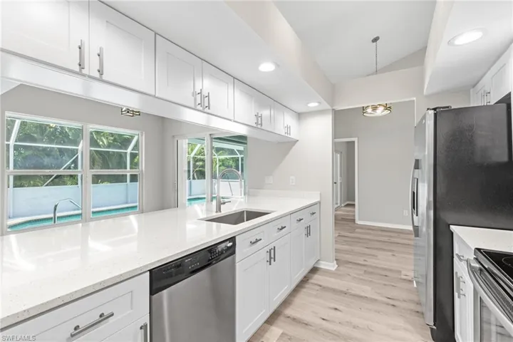 Kitchen with vaulted ceiling, light stone countertops, appliances with stainless steel finishes, sink, and white cabinetry