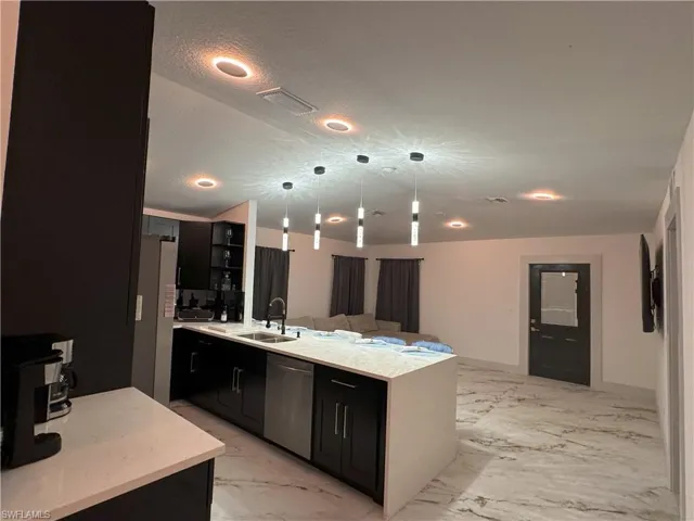 Kitchen with stainless steel dishwasher, sink, refrigerator, light tile patterned floors, and hanging light fixtures