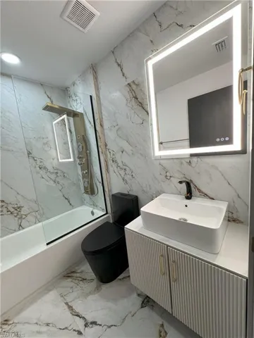Full bathroom with vanity, tile patterned floors, tiled shower / bath, tile walls, and toilet
