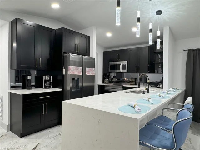 Kitchen with a kitchen bar, appliances with stainless steel finishes, decorative light fixtures, kitchen peninsula, and light tile patterned flooring