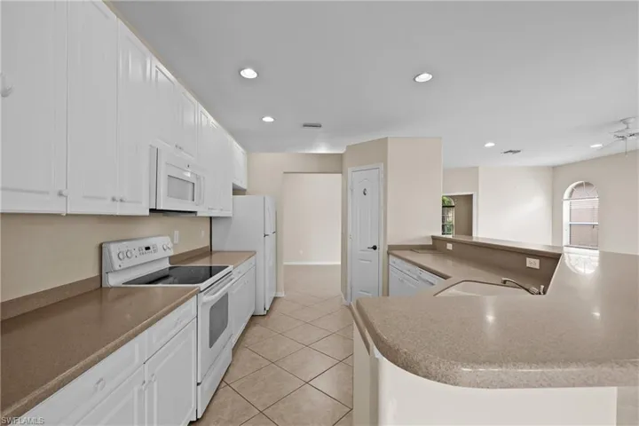 Kitchen with white appliances, white cabinets, pantry, recessed lighting, light tile patterned floors.
