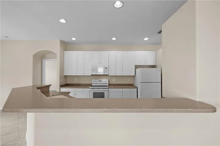 Kitchen featuring white appliances, recessed lighting, white cabinets, light tile patterned flooring, and a kitchen bar