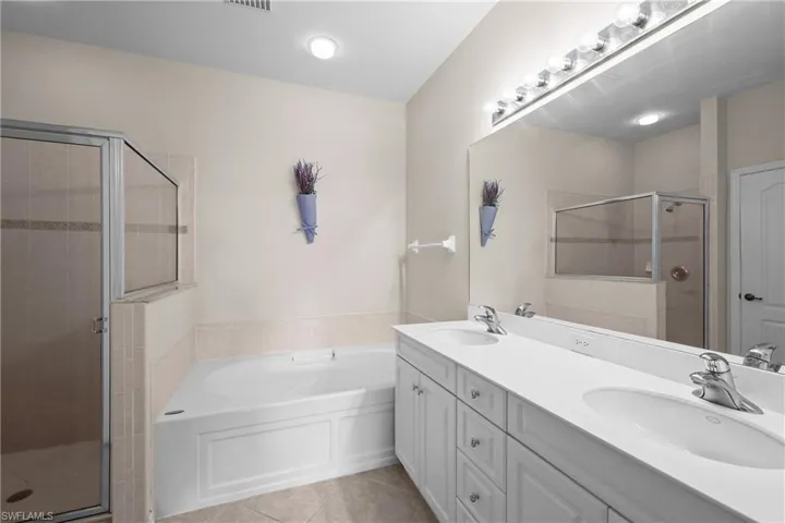 Primary Bathroom with a garden tub, light tile patterned floors, a stall shower, and double vanity