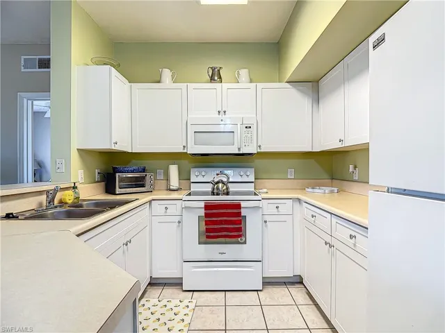 Kitchen featuring white cabinetry, sink, light tile patterned floors, and white appliances