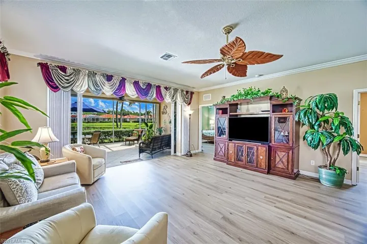 Living room featuring ceiling fan, a textured ceiling, wood-type flooring, and ornamental molding